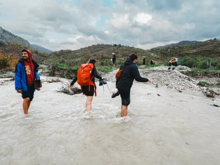 Three people wading across a shallow river in a natural landscape.
