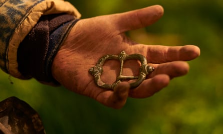 A muddy hand holding a buckle-shaped metal object