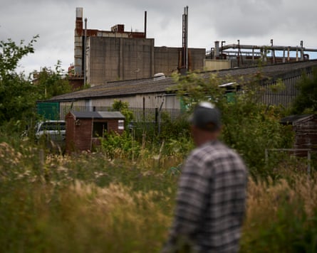 Alan Hodson photographed from behind in a baseball cap and plaid shirt with the AGC Chemicals Europe plant in the background