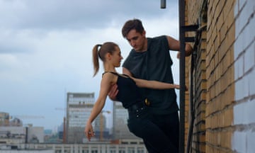 A man and a woman hold onto a ladder and each other as they scale the side of a building