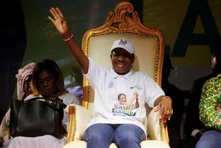 Henriette Lagou Adjoua sits in a high backed gold chair, wearing a white baseball cap, white T-shirt and jeans while waving to a crowd