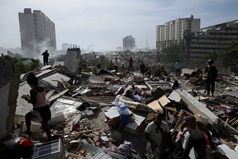 People walk through rubble of collapsed buildings.