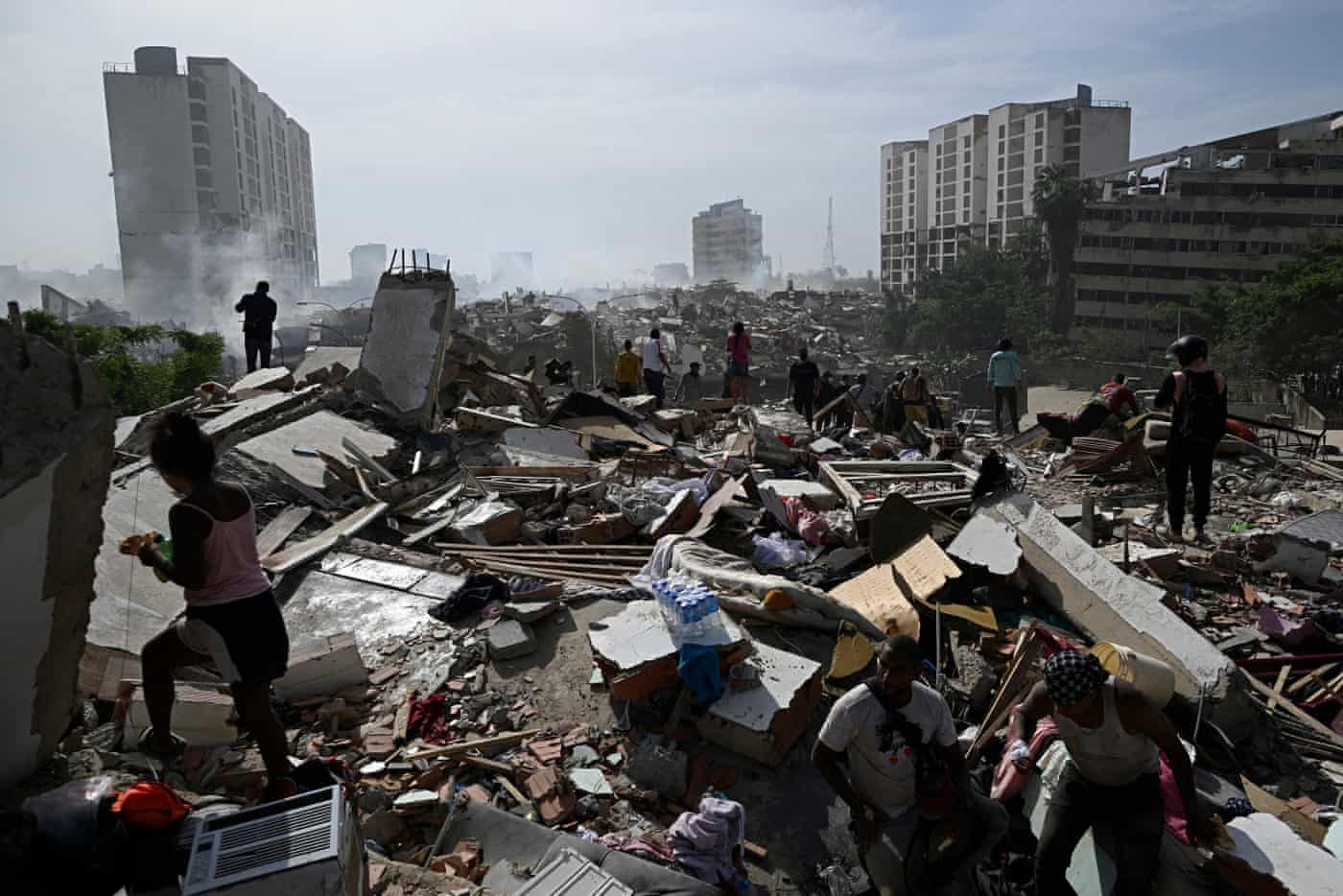 People walk through rubble of collapsed buildings.