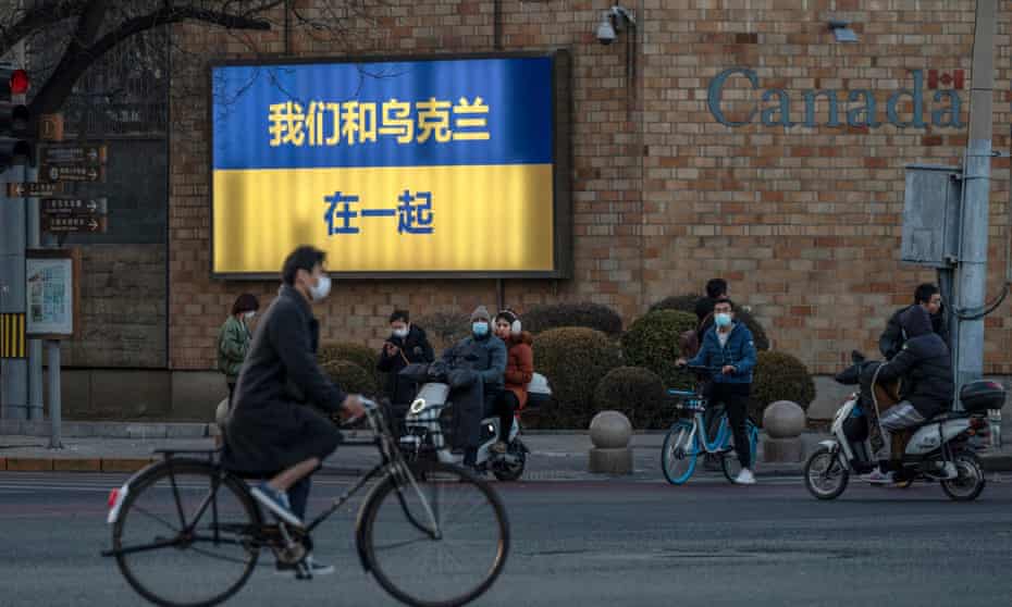 Cyclists pass a Ukrainian flag with the slogan ‘We stand with Ukraine’ written in Chinese characters on a wall outside the Canadian embassy in Beijing