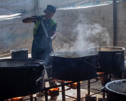 Man stirring a large pot in a community kitchen in a tent