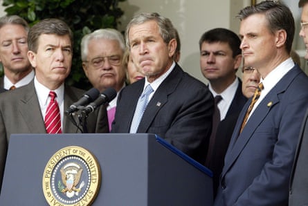 A man frowns at a lectern outside as men stand around him