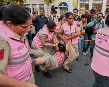 Police in pink vests carry a man by his arms and legs