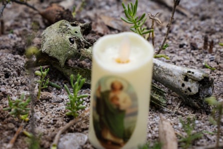 A candle with a illustration of a saint printed on its side next to a human bone on the ground.