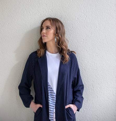 A woman wearing a white top with blue diagonal stripes on the bottom right hand side and a blue cotton jacket looks to her right