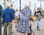 An elderly woman uses a wheeled walking frame along a street