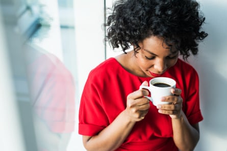 Une femme debout près de la fenêtre tenant une tasse de café