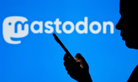 The Mastodon logo seen in the background of a silhouetted woman holding a mobile phone. 