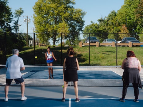 A woman stands on one side of a pickleball court facing three people on the other side of the net.