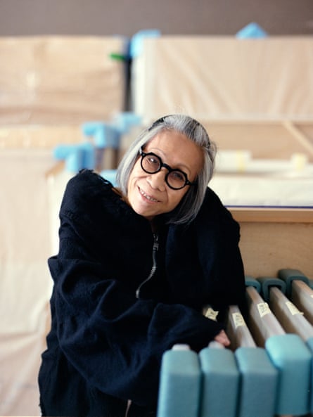 A woman wearing round glasses poses next to artwork