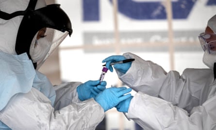 Health workers dressed in personal protective equipment (PPE) handle a coronavirus test at a drive-thru testing station at Cummings Park on March 23, 2020 in Stamford, Connecticut. Availability of protective clothing for medical workers has become a major issue as COVID-19 cases surge throughout the United States. The Stamford site is run by Murphy Medical Associates.