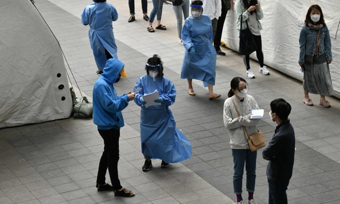 Medical staff members (in blue gowns) wearing protective clothing guide visitors at a virus testing station in the nightlife district of Itaewon in Seoul on 12 May 2020.