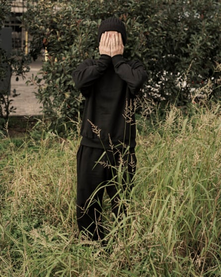 A man stands in tall grass with his hands covering his face