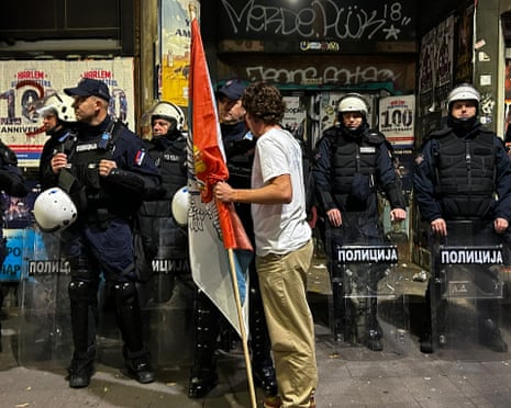 A man holds a flag while speaking closely with a riot police officer during a Belgrade street celebration