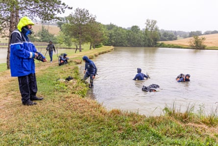 Men in scuba equipment emerge at the surface of a lake while a policeman looks on