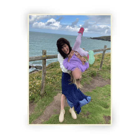 Matilda Davis hold a child, face blurred, upside down on a path next to the sea