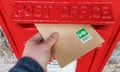 Hand posting a letter with a barcoded stamp into a red letterbox