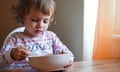 A two-year-old girl eats cereal at a table