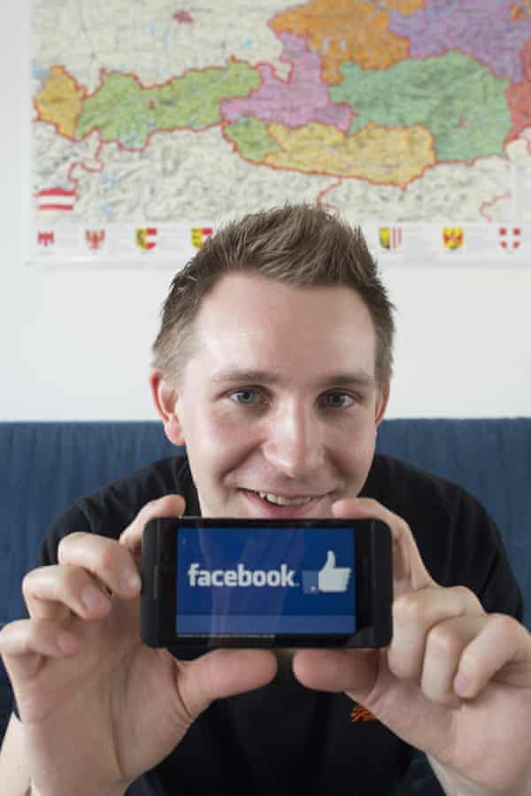 Max Schrems holds up a smartphone with the Facebook app on it.