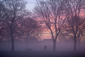 Ilford, UK. A pedestrian walks through the mist in a park in east London