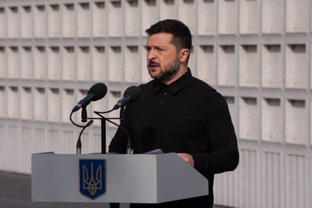 Volodymyr Zelenskyy speaks at an event in front of a white wall. He is wearing black.
