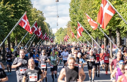 Marathon runners pass down a tree-lined street with Danish flags