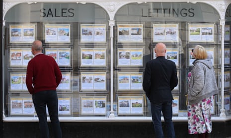 People looking at house price signs in the window of an estate agent's.