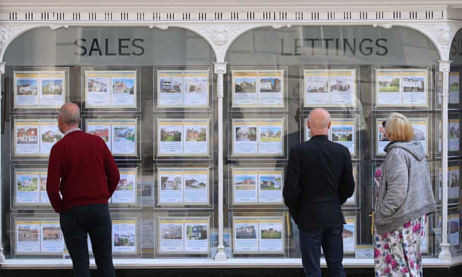 People looking at house price signs displayed in the window of an estate agents.