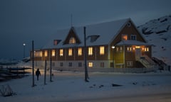 A two-storey building in a snowy landscape with a steeply pitched roof  and all its windows aglow with light