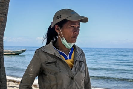 A worried-looking woman in a peaked cap and wearing a face mask stands on a beach