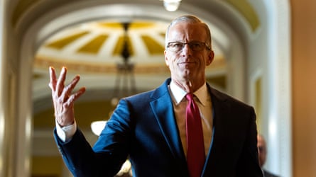 John Thune gestures while walking through a corridor in the Senate
