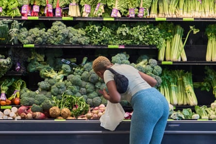Woman leans into vegetable cooler looking at broccoli.
