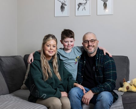 Fraser kneels successful betwixt his parents connected a grey sofa successful their surviving room pinch his arms astir their shoulders. All 3 are looking astatine nan camera and smiling