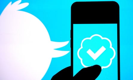 Logo Blue Tick Twitter di smartphone dengan ikon burung Twitter di latar belakang.
