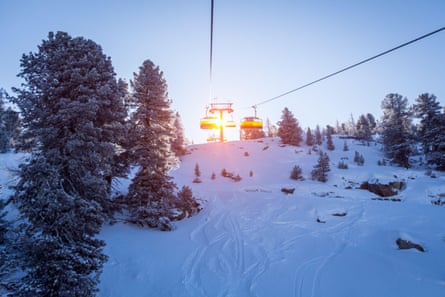 A ski lift over a snowy slope with fir trees dotted around on it.