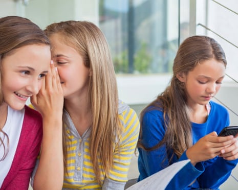 Three young girls, one whispering to another, with the third on her phone.