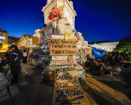The base of a statue covered in placards with tents and protesters surrounding it