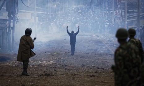 FILE - In this Thursday, Aug. 10, 2017 file photo A man seeking safety walks with his hands in the air through a thick cloud of tear gas towards riot police, as they clash with protesters throwing rocks in the Kawangware slum of Nairobi, Kenya on 10 August
