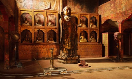 A movie set, with a large religious figure, it's hand in the air, in the centre of shot. In the foreground a film accessory, a dolly, sit on some track.