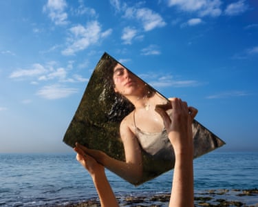 woman’s reflection seen as she holds up mirror by water