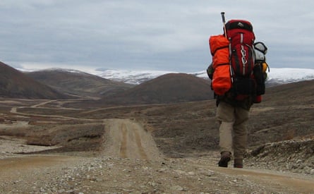 Wearing a huge rucksack, he treks across a lifeless brown plain with snowy mountains in the distance
