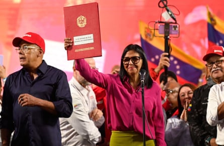 ديلسي رودريغيز ترفع مجلدًا جلديًا أحمر منقوشًا يحتوي على القانون الجديد. يقف مؤيدون على خشبة المسرح خلفها وشقيقها