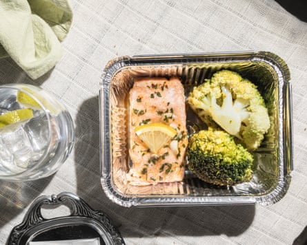 Overhead shot of a finished baked salmon meal at a restaurant, with leftovers packed to go in a doggy bag, emphasising zero waste and food reuse