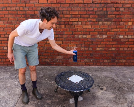 Pete Wise holds a blue coffee up over a small black iron table with a piece of kitchen paper on it to check if any drips come from the cup