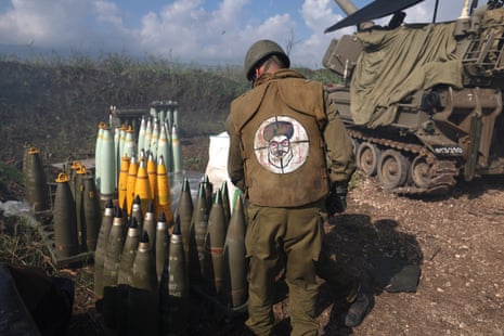 An Isareli soldier wearing a jacket with crosshairs and a cartoon of Lebanese Hezbollah leader Hassan Nasrallah prepares to fire artillery shells towards a target in Lebanon from an undisclosed location in northern Israel