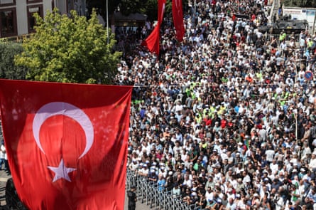 Street filled with crowds seen from above, with red and white Turkish flag.